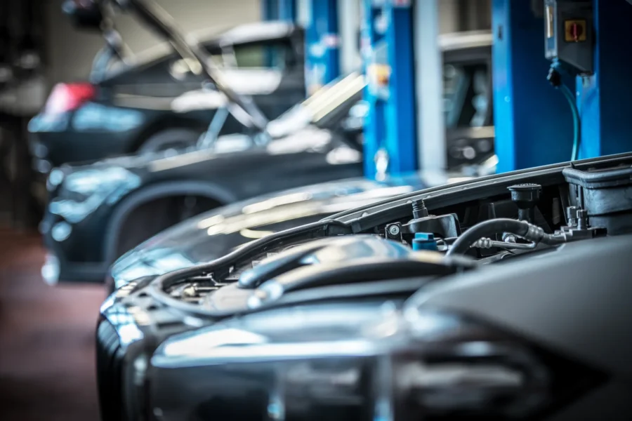 Two cars with their hoods open inside an auto repair shop, with blue vehicle lifts in the blurred background.