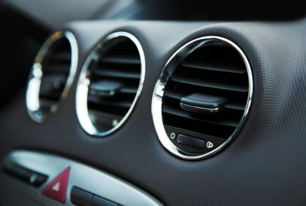 Close-up of three round chrome-trimmed air conditioning vents on a car's dark grey dashboard.