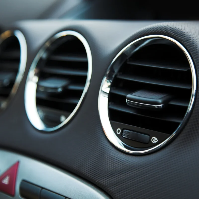 Close-up of three round chrome-trimmed air conditioning vents on a car's dark grey dashboard.